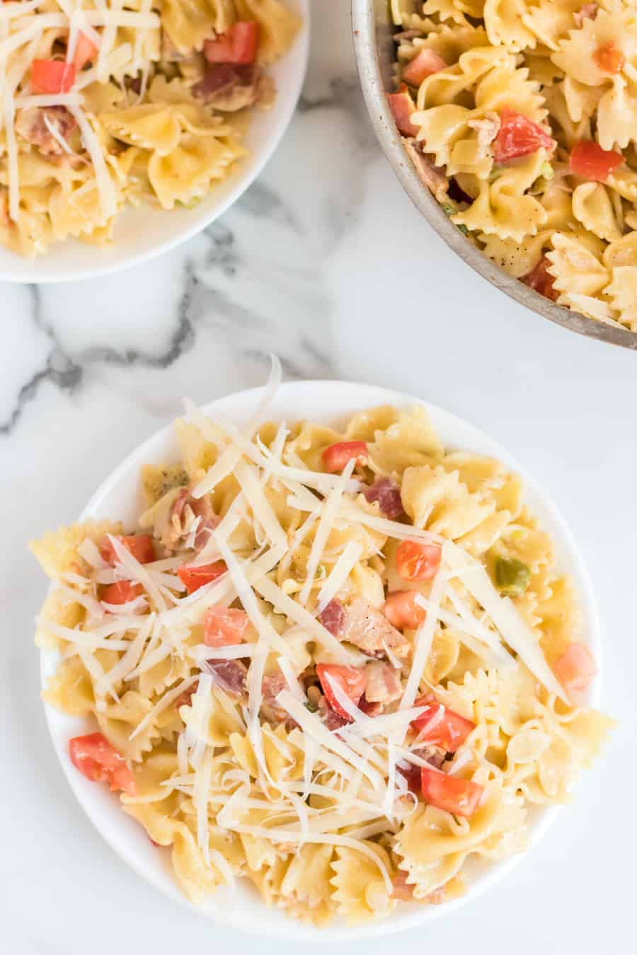 Pasta with bacon, tomatoes, green peppers, and shaved Parmesan cheese on a white plate.