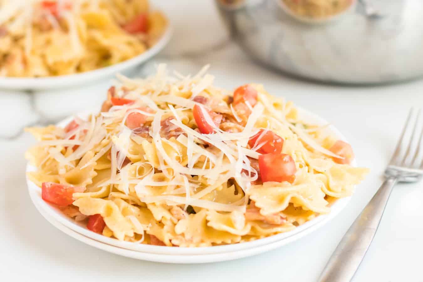 Pasta with bacon, tomatoes, green peppers, and shaved Parmesan cheese on a white plate.