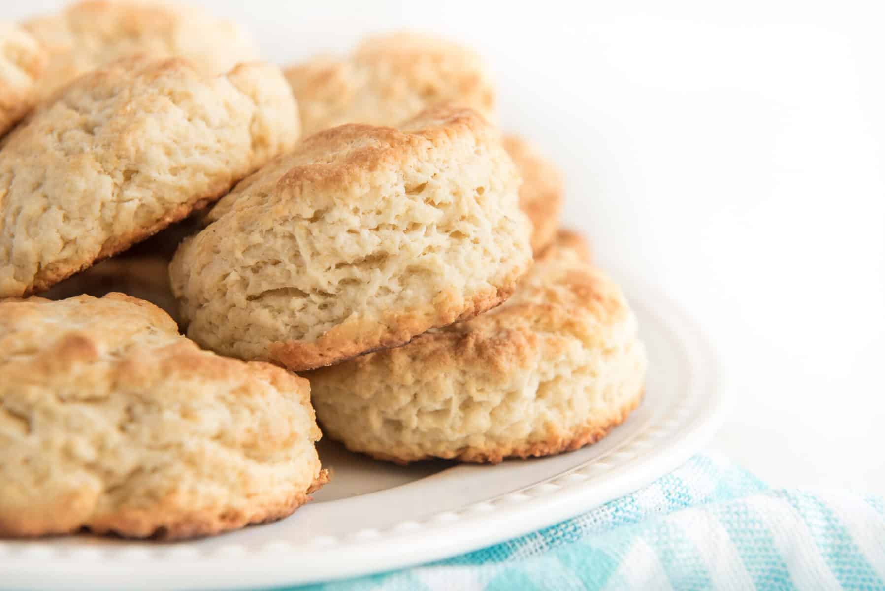 white plate with several biscuits in a pile blue and white dish towel underneath.