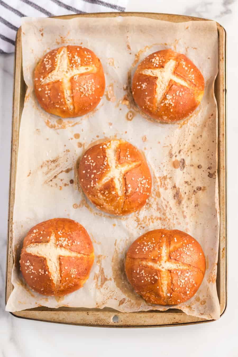 an overhead shot of five pretzel rolls sitting on a sheet pan lined with parchment paper.