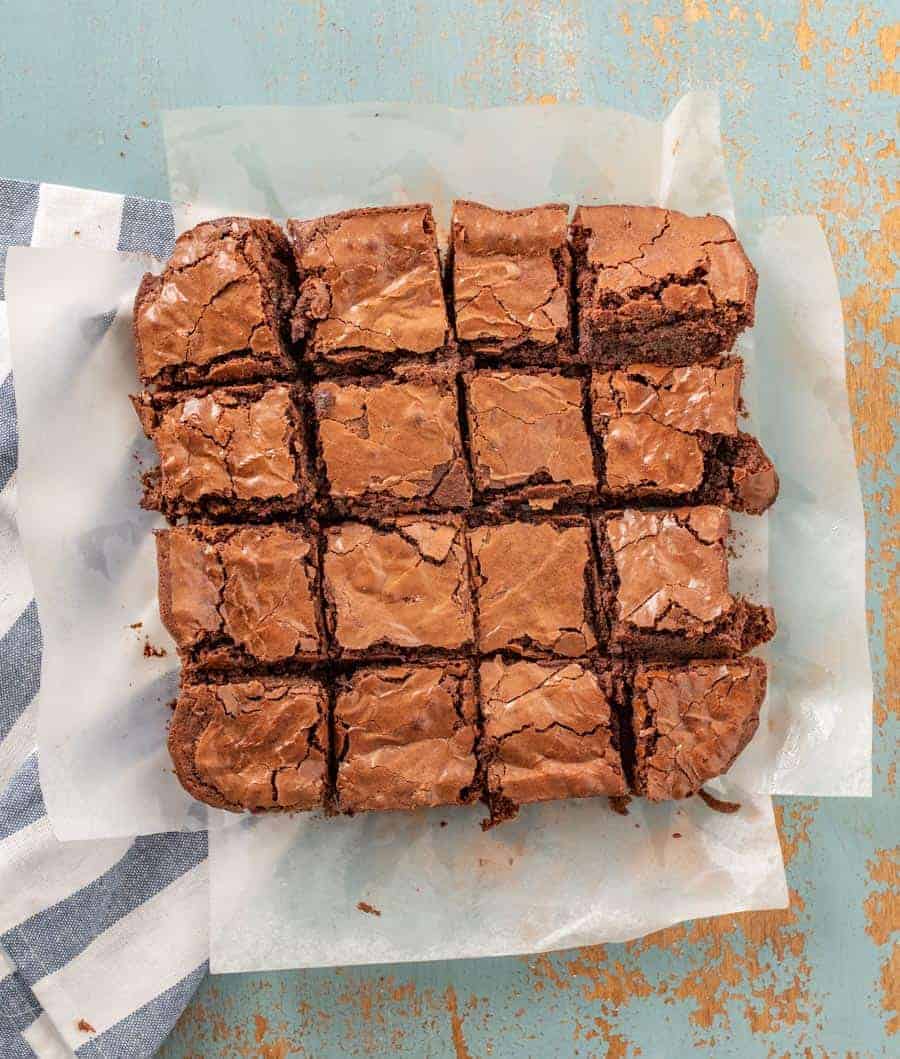 A pan of brownies cut into 16 on a piece of white parchment paper.
