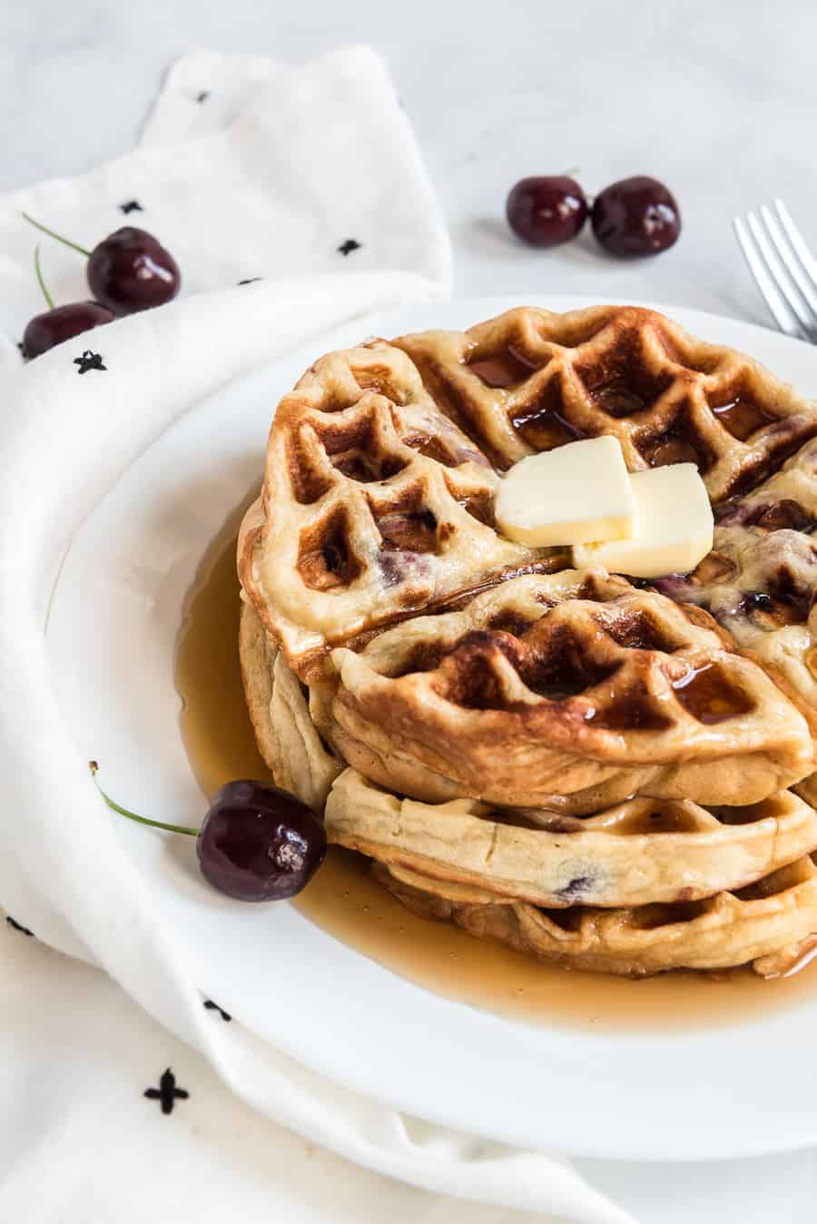 sweet cherry waffles with butter on top on a white plate.