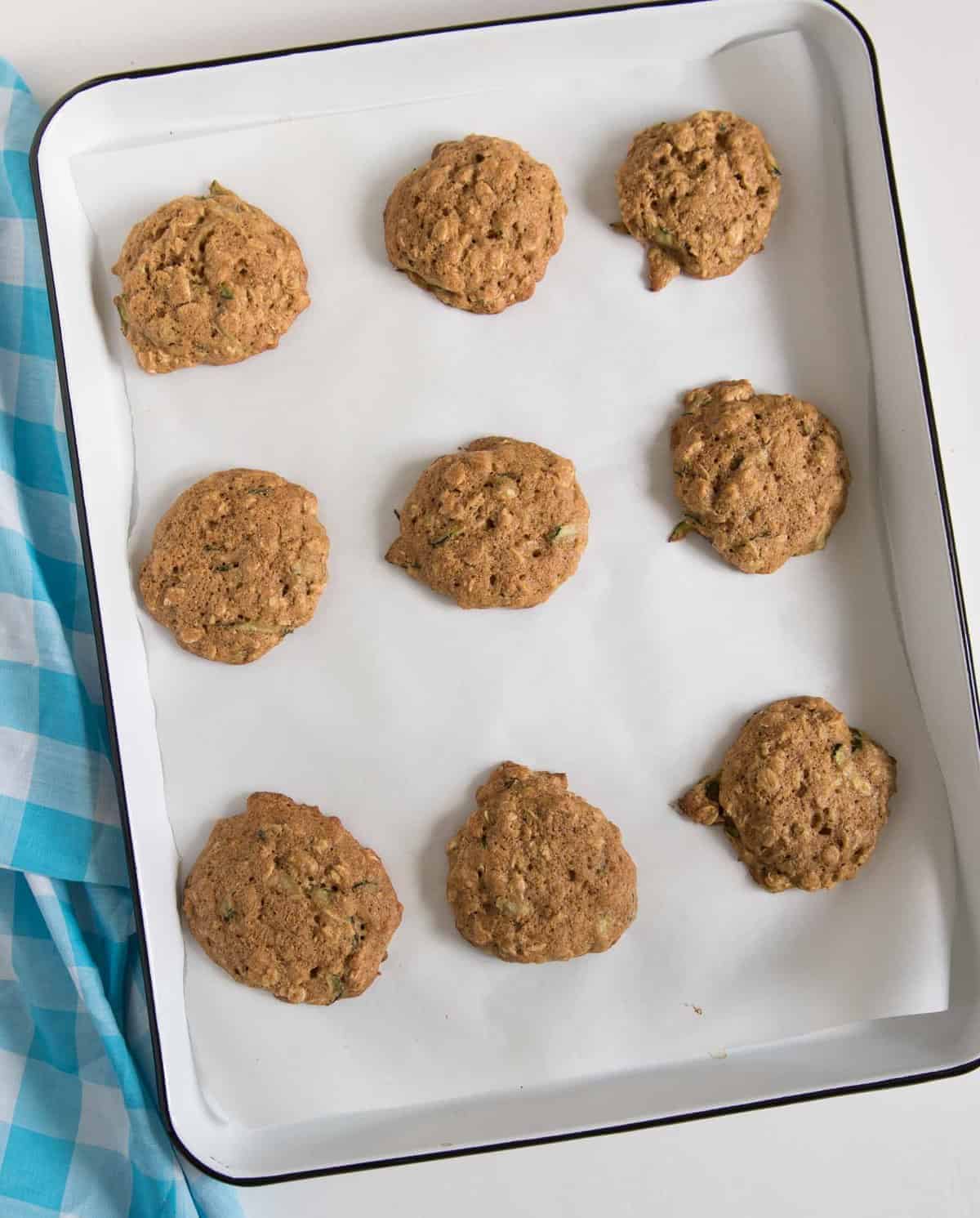 Nine baked zucchini oatmeal cookies resting on a white rimmed baking sheet with a black rim.