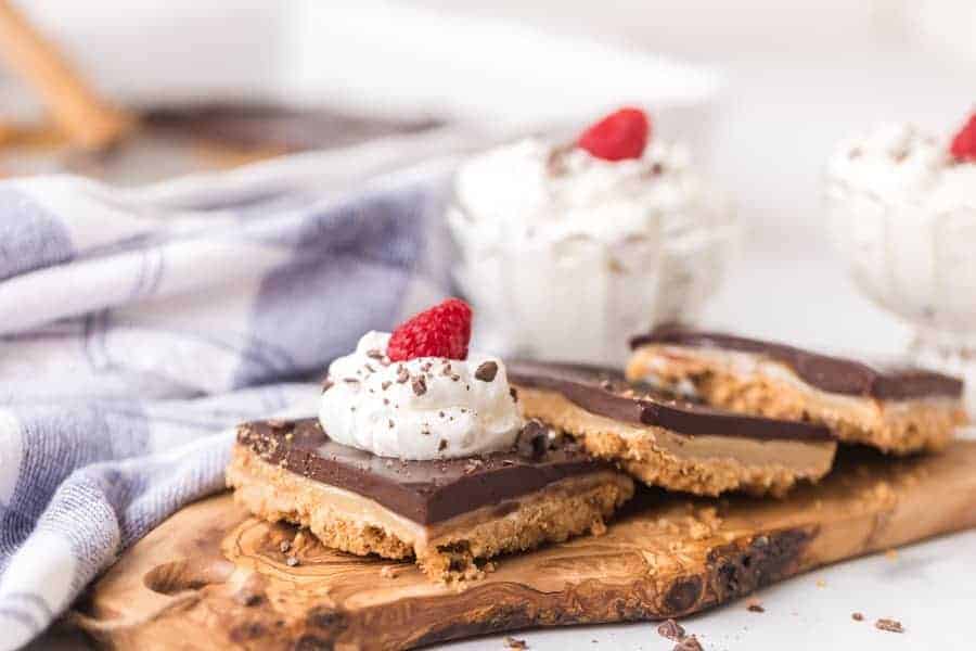 gooey chocolate caramel tart dessert with whipped cream and a raspberry on top on wooden cutting board.