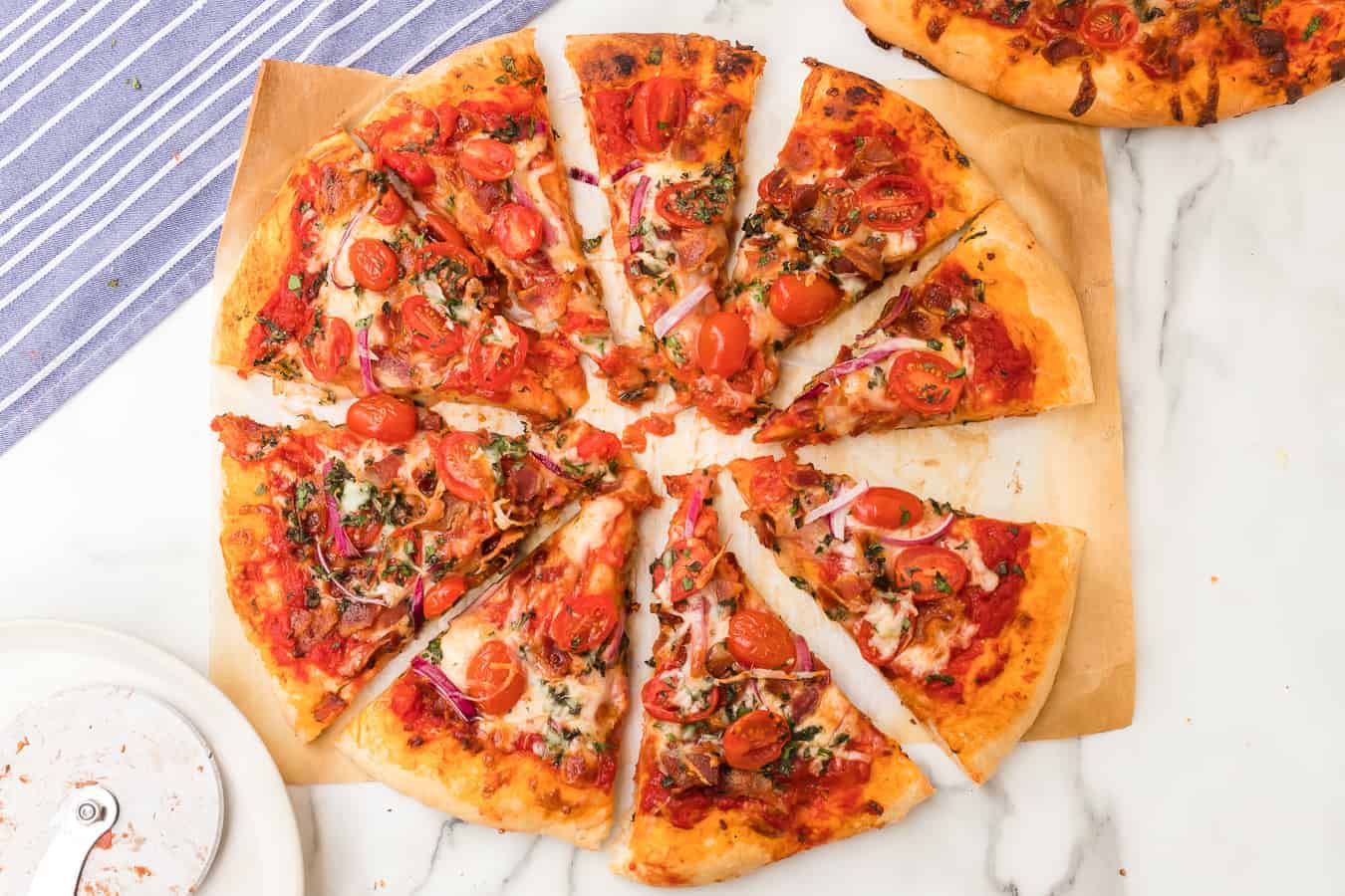 baked pizza dough with sauce, mozzarella, red tomatoes, green herbs, and red onion toppings on a white parchment.