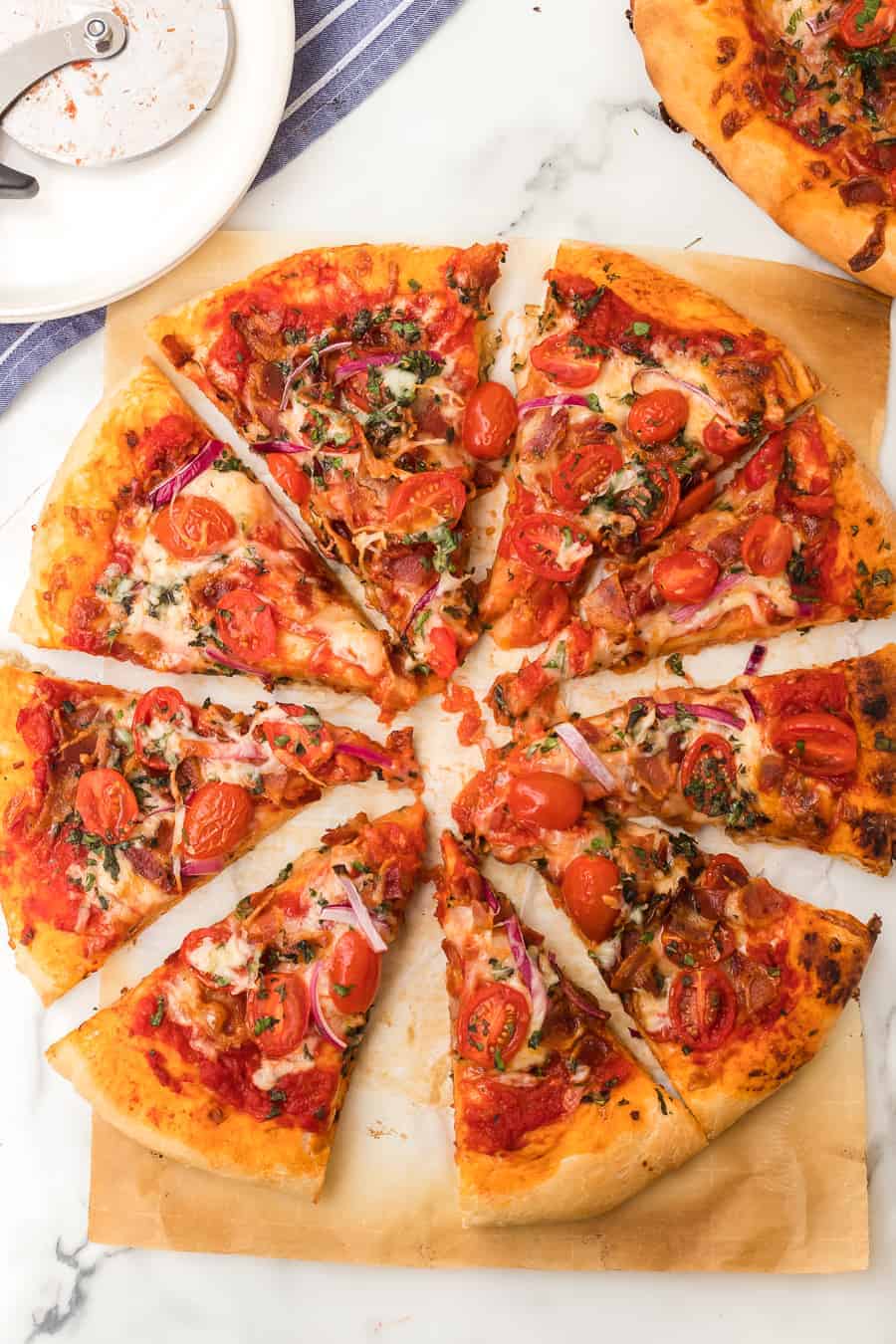 a whole herbed tomato and bacon pizza on parchment.