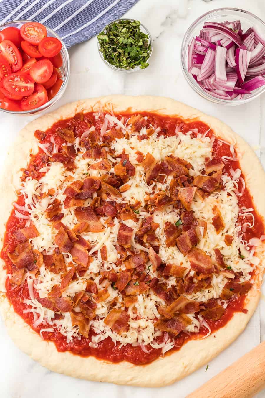 a raw a whole herbed tomato and bacon pizza on parchment.