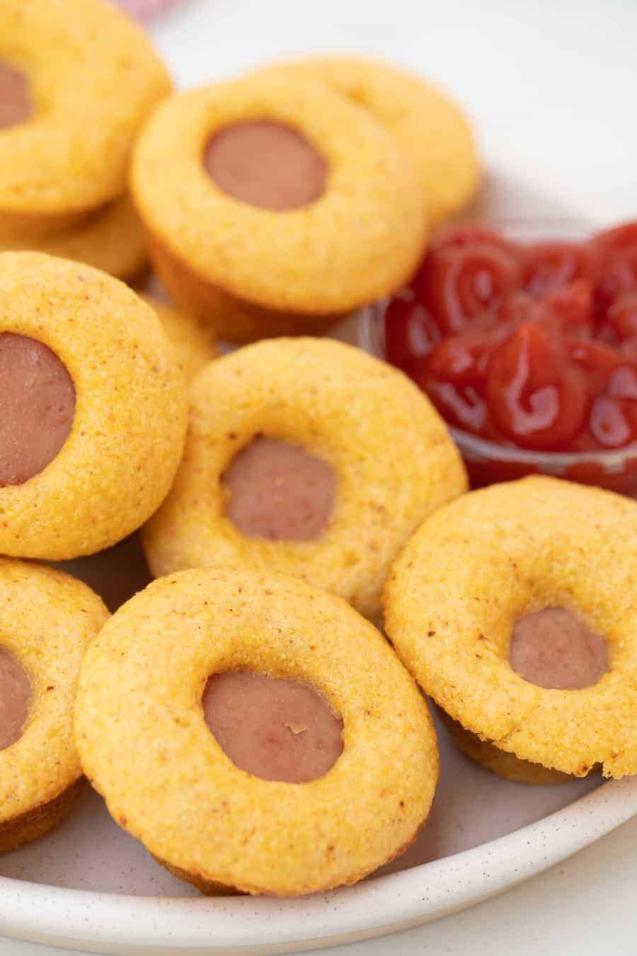 small bites of cornbread with pieces of hotdog inside on a white plate.