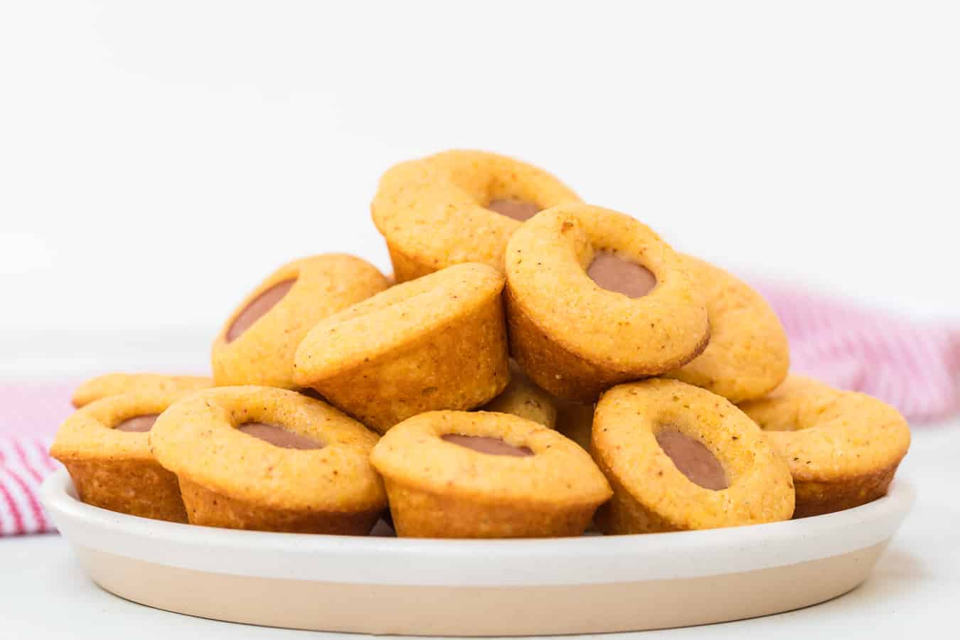 small corn muffins with pieces of hotdogs in them on white plate.