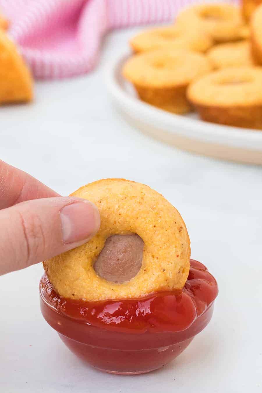 a small muffin shaped corn dog POV in a hand being dipped into ketchup.