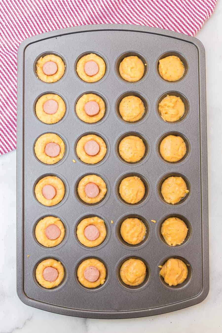 a muffin tin with cornbread mix and hot dogs inside - baked.