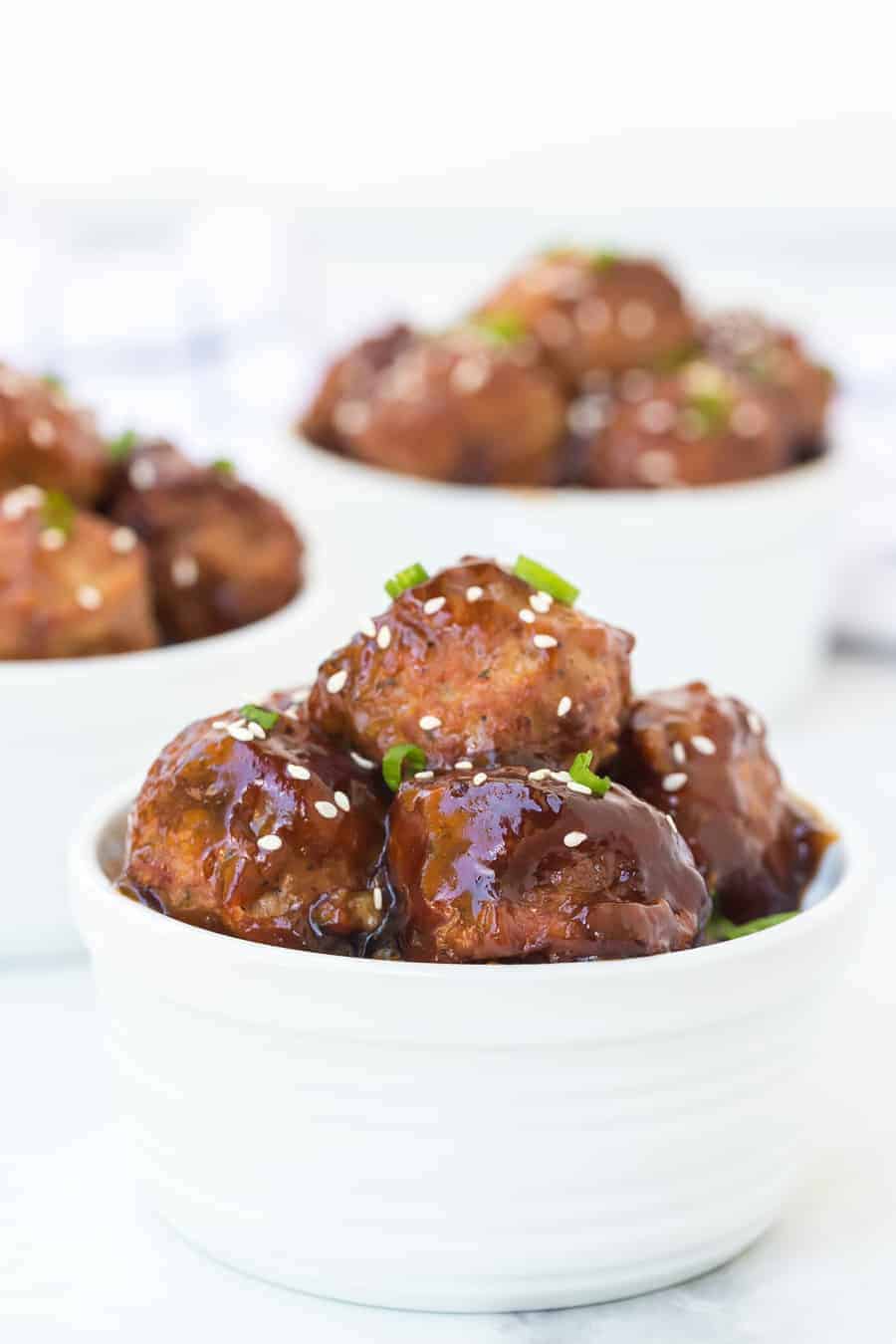 sweet savory meatballs topped with sesame seeds and green onions in white ramekin.