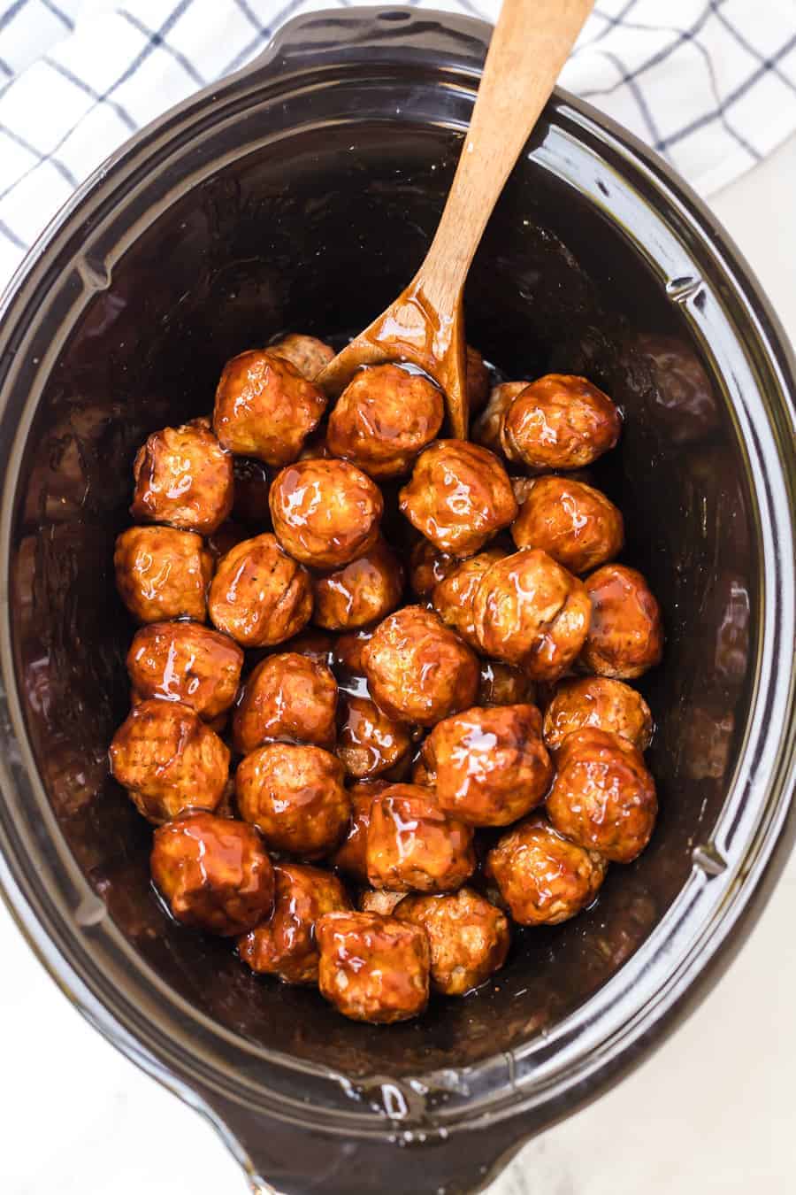 Honey Teriyaki Meatballs in a black crockpot with wooden spoon.