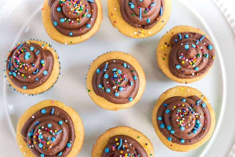 Vanilla cupcakes with chocolate frosting and rainbow sprinkles, overhead view.