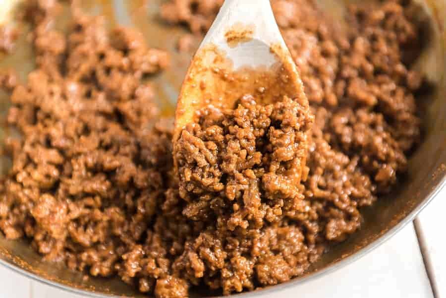 ground beef mixture in metal pan with white wooden spoon holding a scoop.