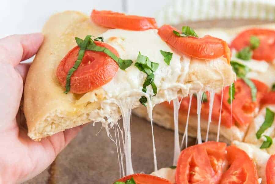 cooked margherita pizza with hand pulling slice off pizza and cheese stretching.