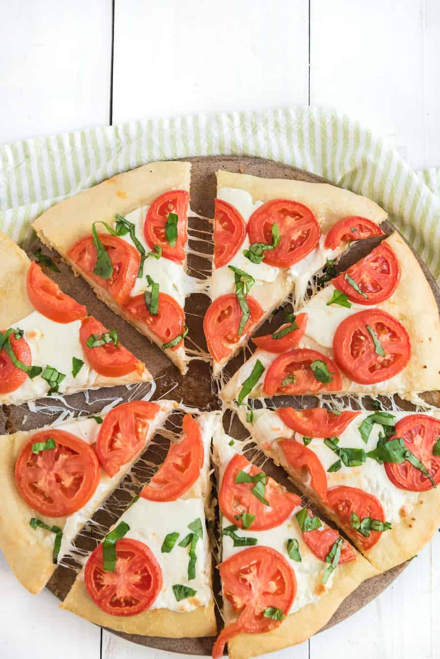cooked margherita pizza on board with tomatoes, basil, and mozzarella cheese on top.