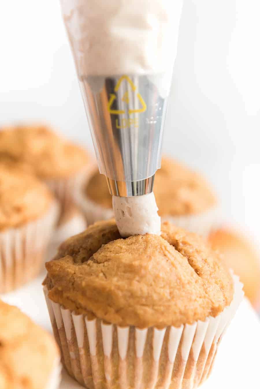 golden colored baked pumpkin cupcakes being iced with a piping bag.