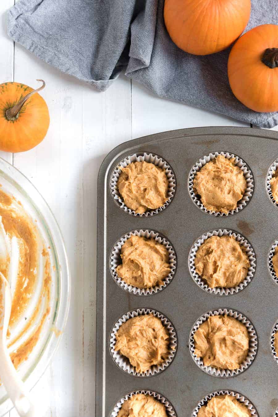 Cupcake pan with batter filled liners in it, and an empty glass mixing bowl beside it.
