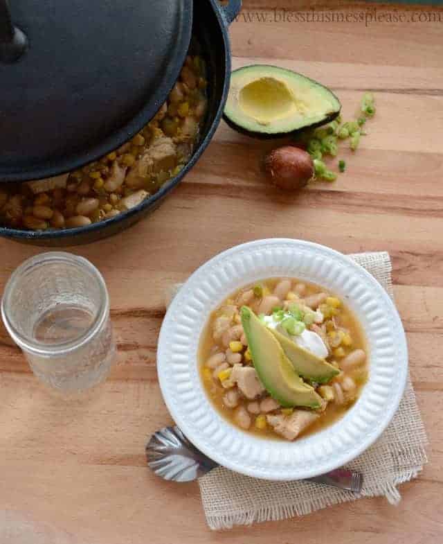 Image of a white bowl with white chicken enchilada soup garnished with two avocado slices, some sour cream, and sliced green onions.