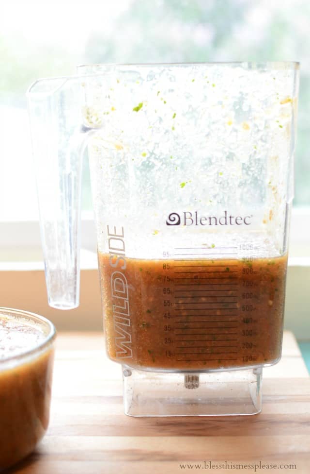 a blender jar about 1/3 full of salsa with a full bowl of blender salsa sitting to the left hand side