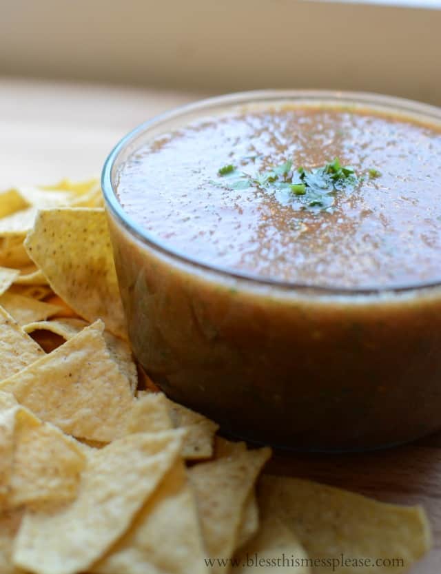 an angle view of a clear bowl full of blender salsa with a pile of yellow tortilla chips to the left of it