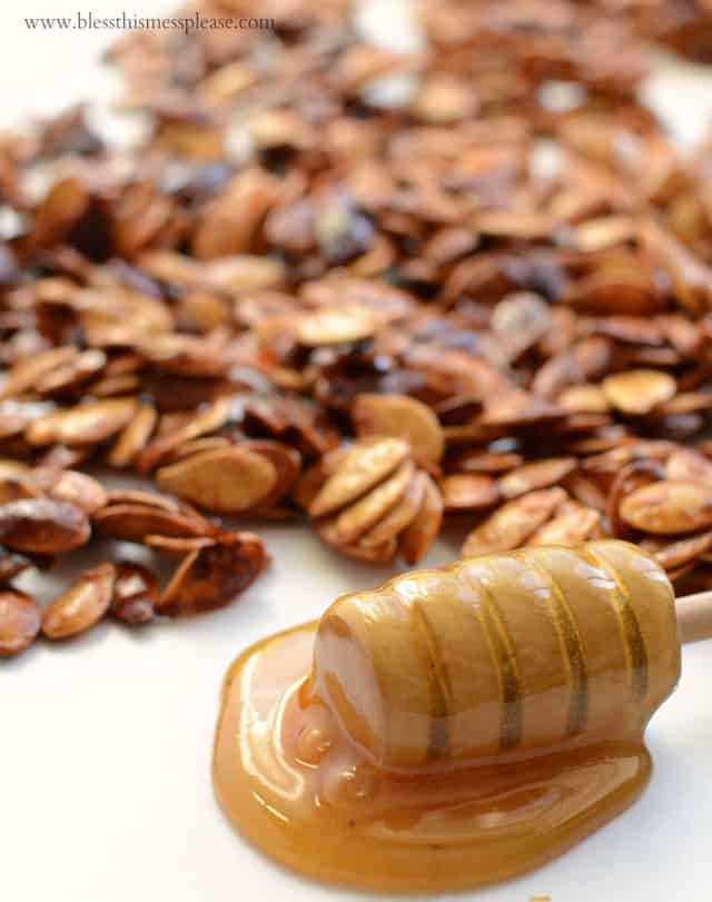 Close up of a honey wand covered in honey next to pumpkin seeds.