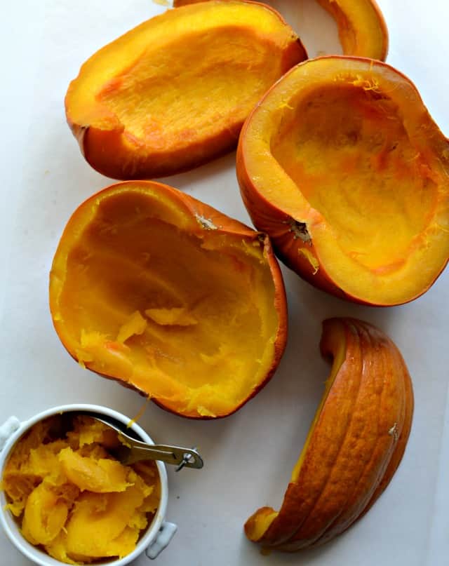 Top view of a slow cooked pumpkin on a counter with the innards being scooped into a bowl.