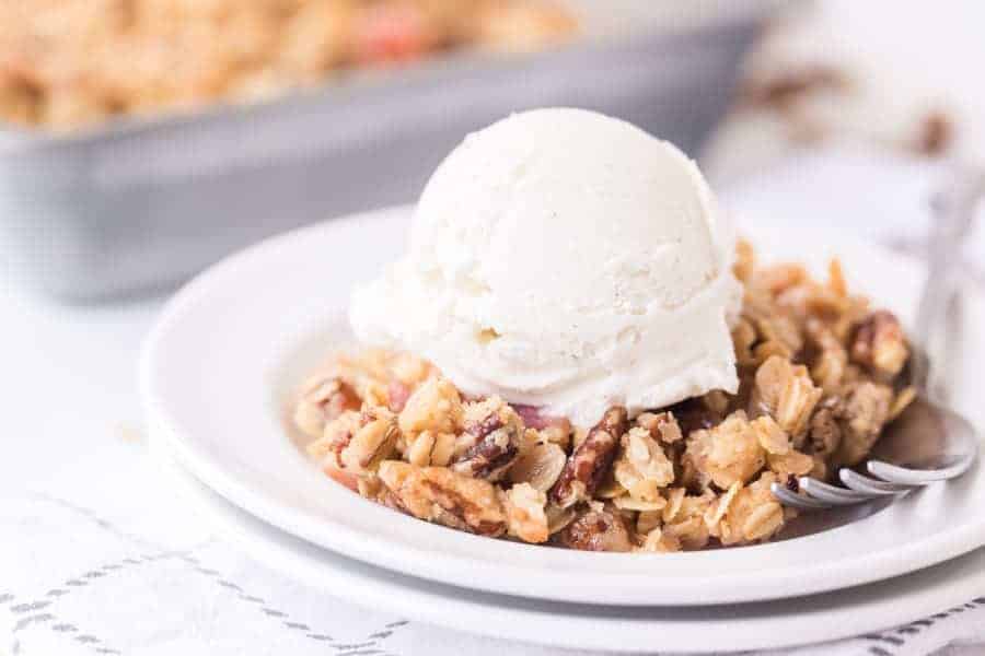 closeup of homemade rhubarb crisp on white plate with scoop of vanilla ice cream