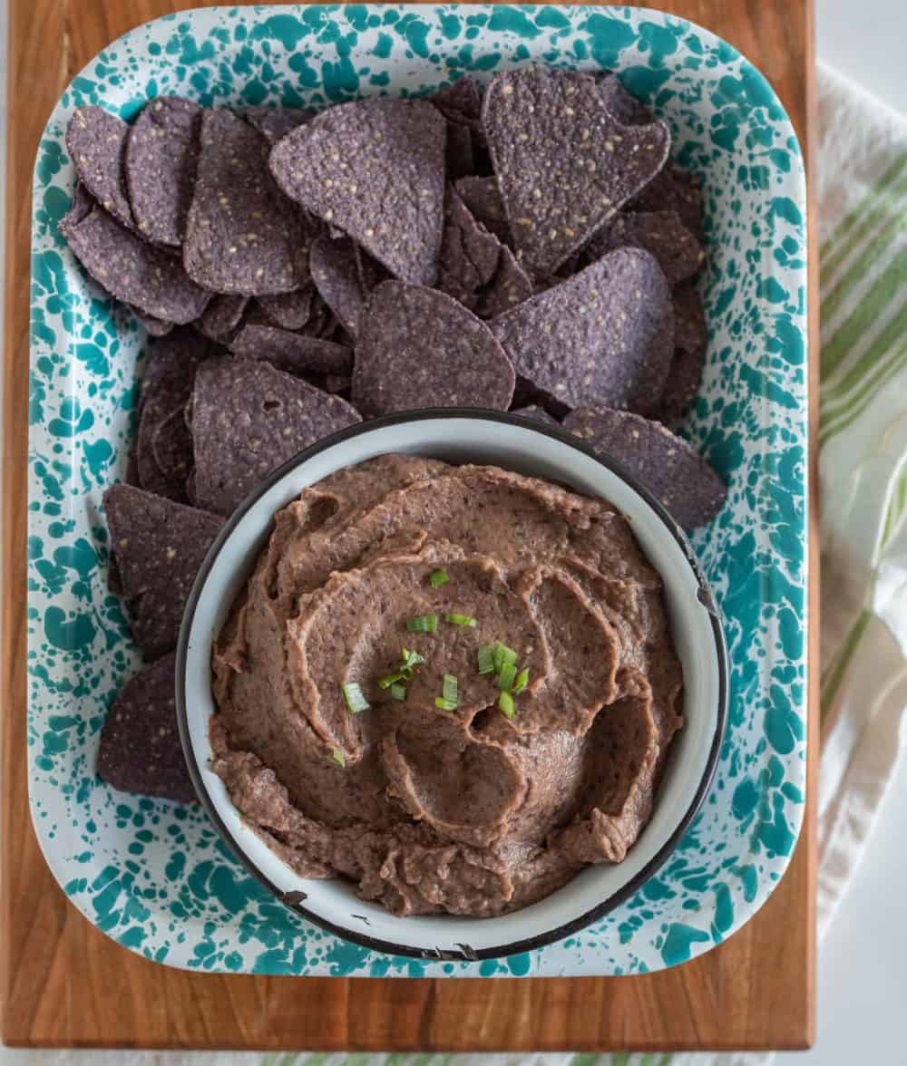 a blue and white tray with a bowl of black bean dip and a pile of blue corn tortilla chips