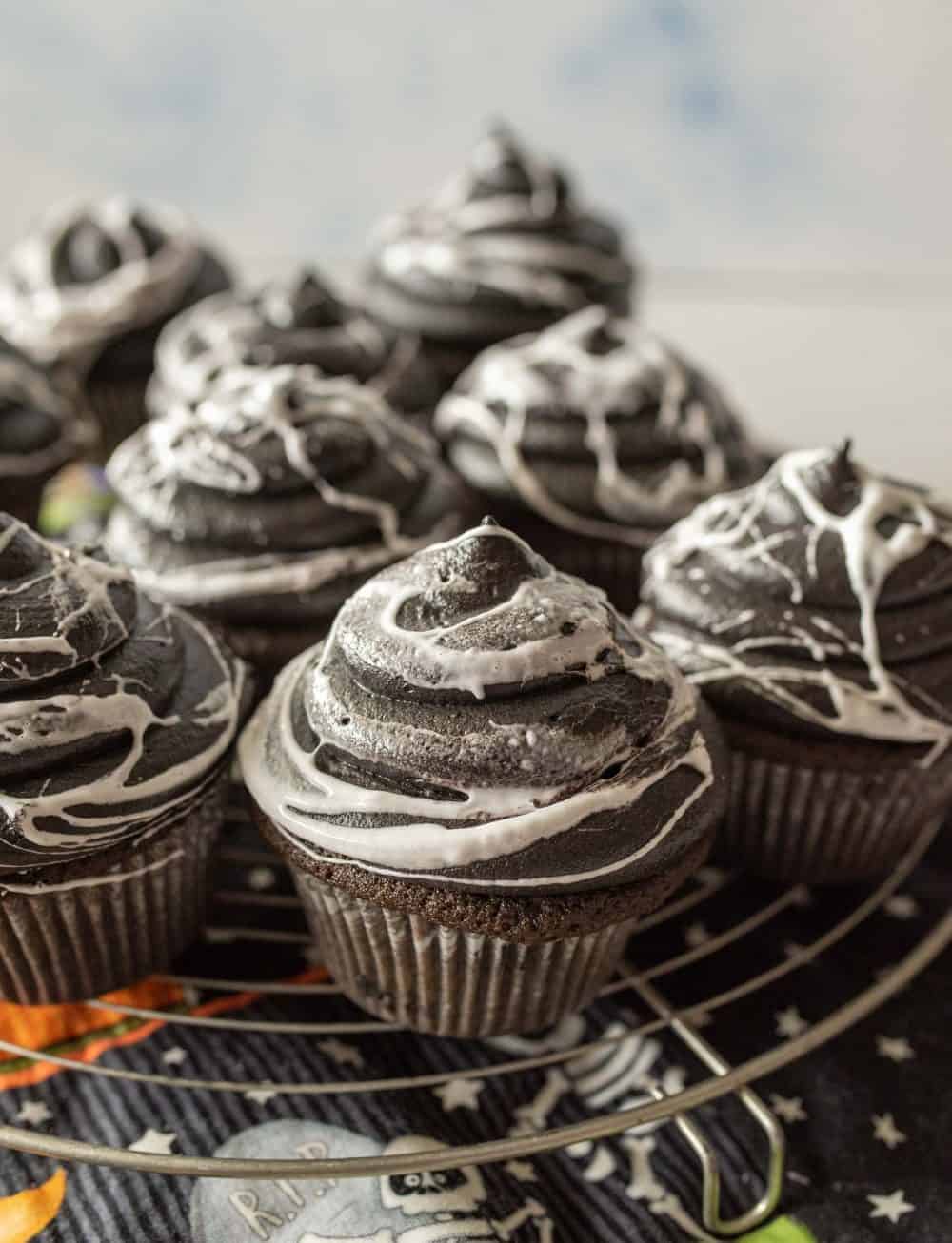 several spider web cupcakes on a cooling rack