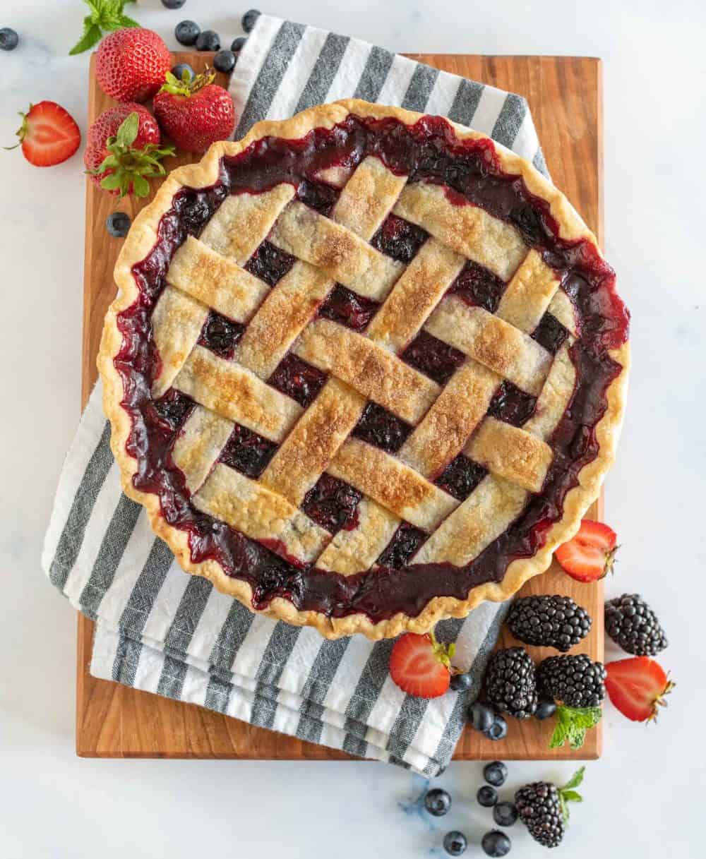 picture of mixed berry pie on a wood board with fresh berries in front.