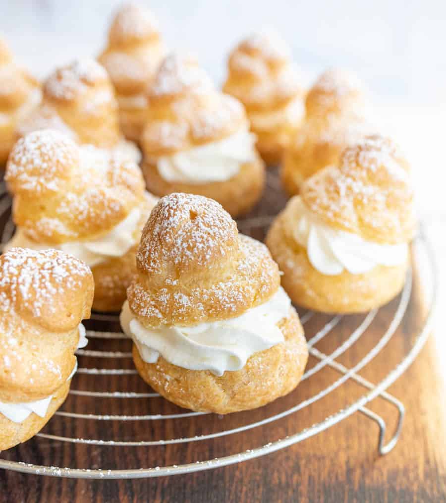 Close up of cream puffs dusted with powdered sugar on a cooling rack.