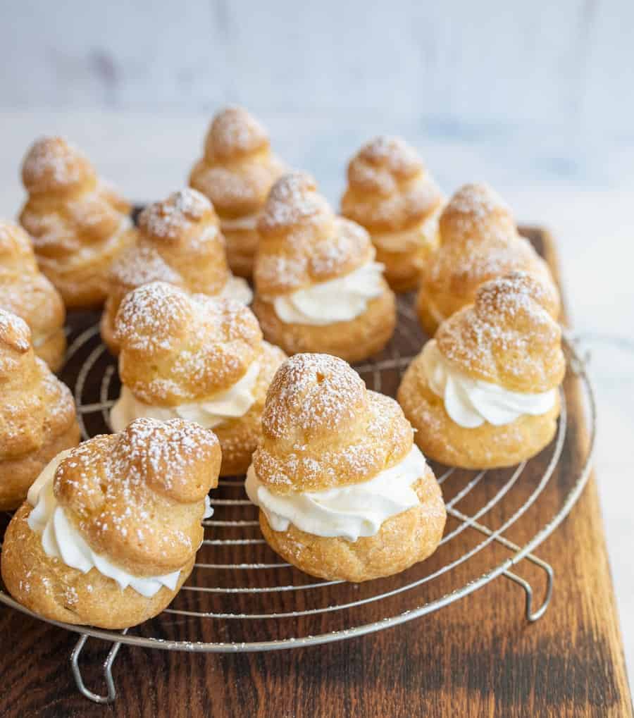 Cream puffs dusted with powdered sugar on a cooling rack.