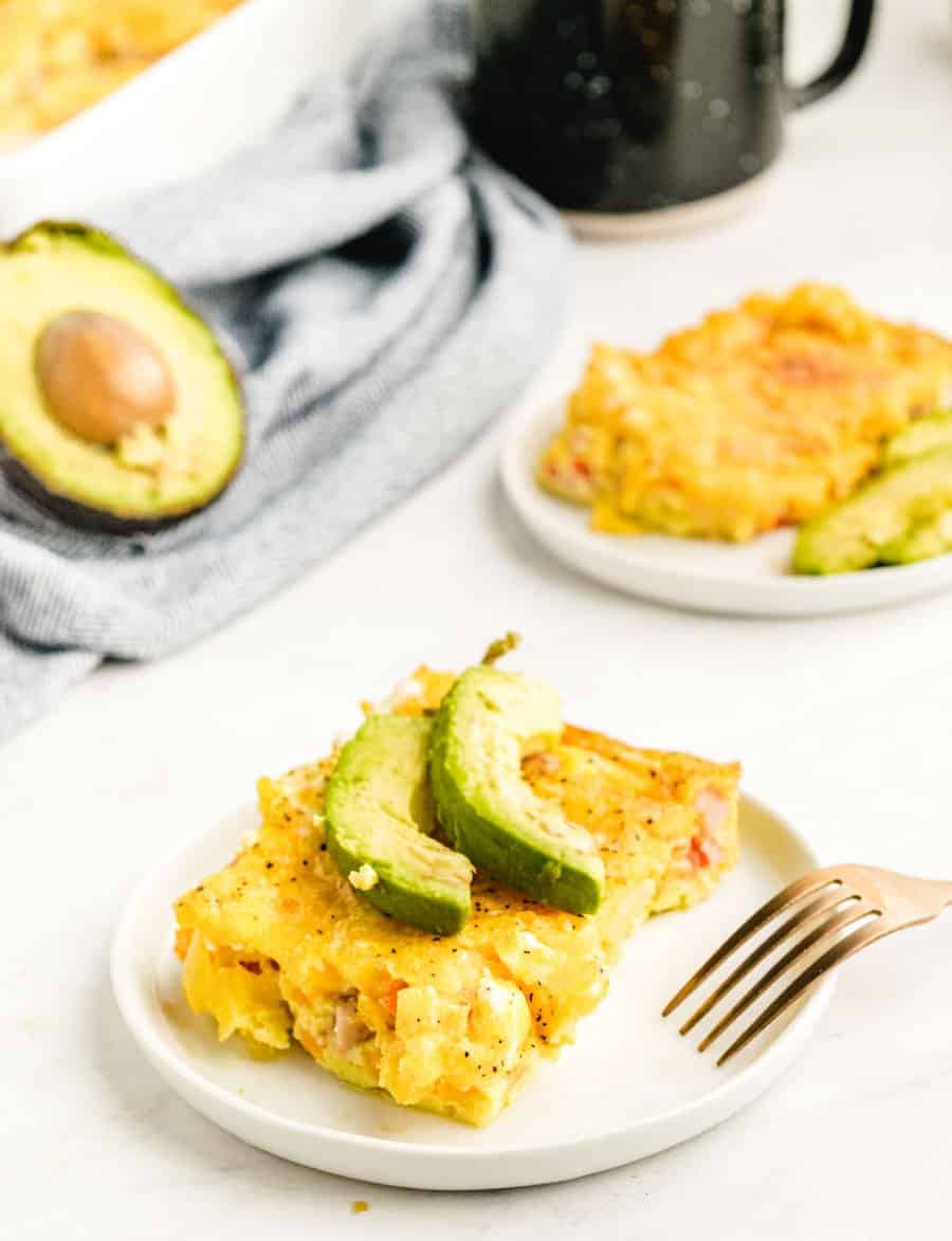 A close up view of a serving of Denver Omelet on a white plate with avocado on top.