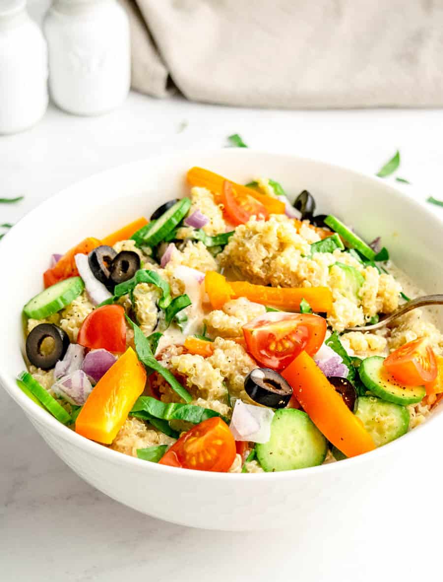 An up close shot of a white bowl of greek quinoa salad.
