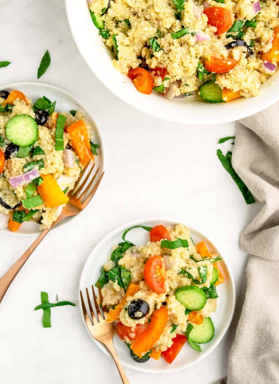 A top view of two white plates of quinoa salad next to the main bowl.