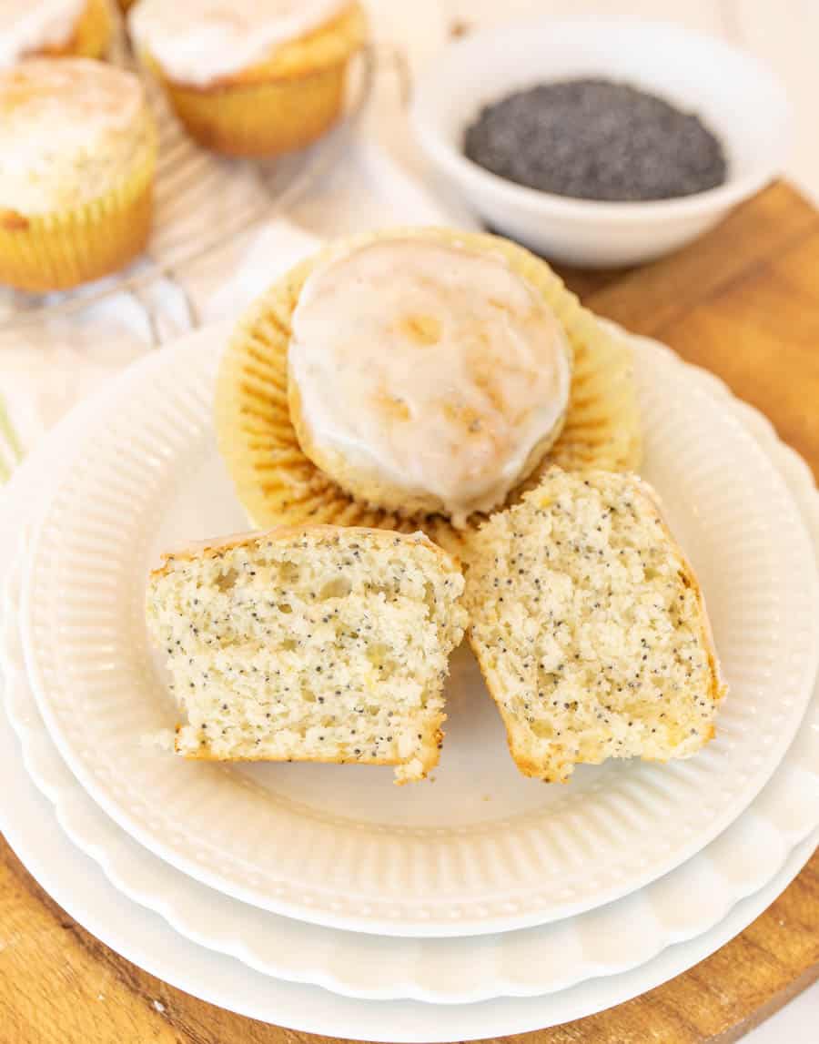 A picture of a lemon poppy seed muffin cut in half and another lemon poppy seed muffin on a plate.