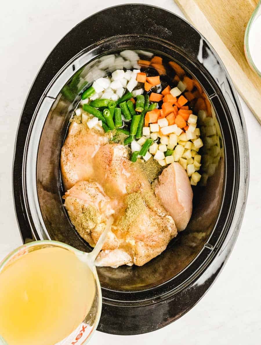 Top view of ingredients for slow cooker chicken pot pie in a slow cooker with broth being poured into it