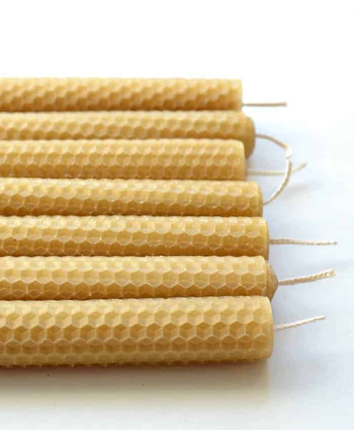 Seven Simple DIY Beeswax Candles lined up in a row on a white countertop.