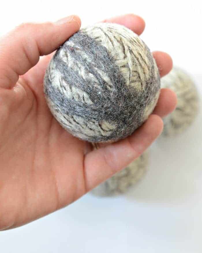 A hand holding a felted wool dryer ball.