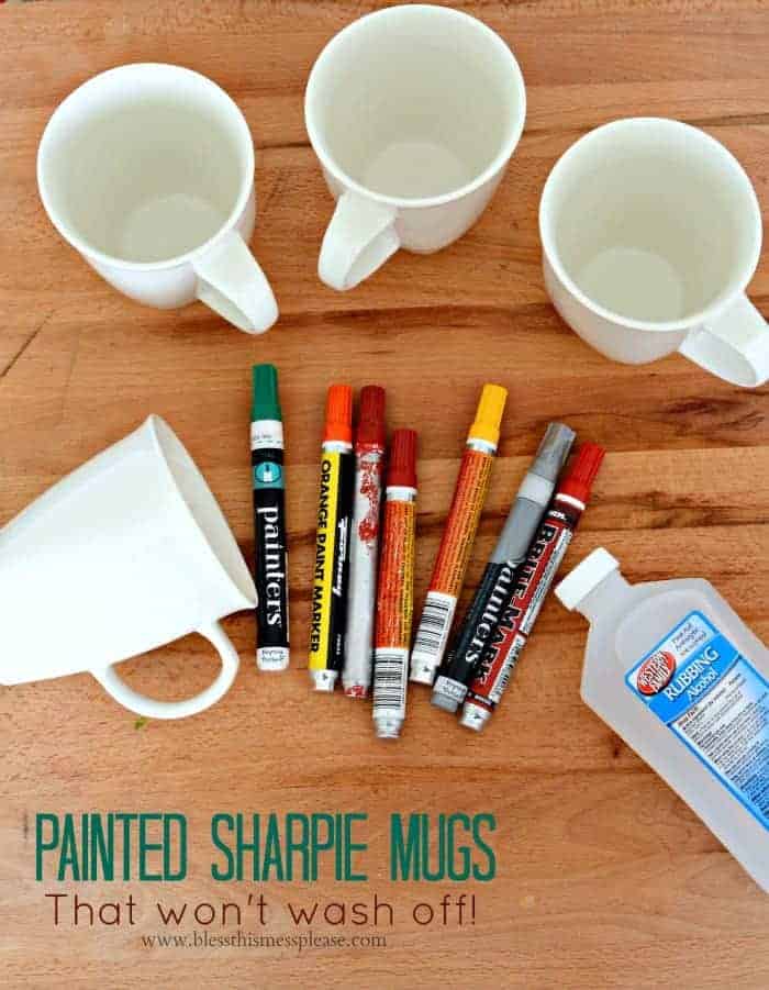 The supplies to make painted sharpie mugs, including some oil-based paint markers, four plain white mugs, and a bottle of rubbing alcohol.