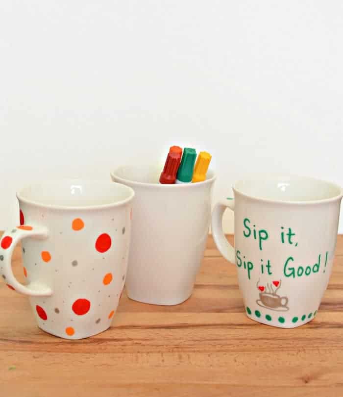 Three painted sharpie mugs on a wooden counter.