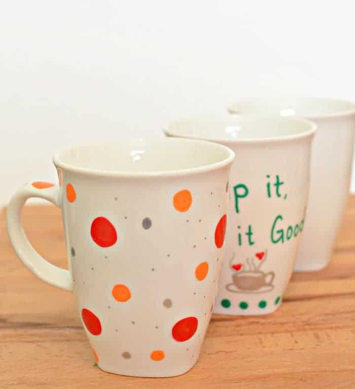 Three painted sharpie mugs in a diagonal line on a wooden counter.