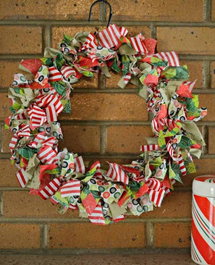 DIY Christmas Rag Wreath made from red, green, and white fabrics hanging on a brick wall.