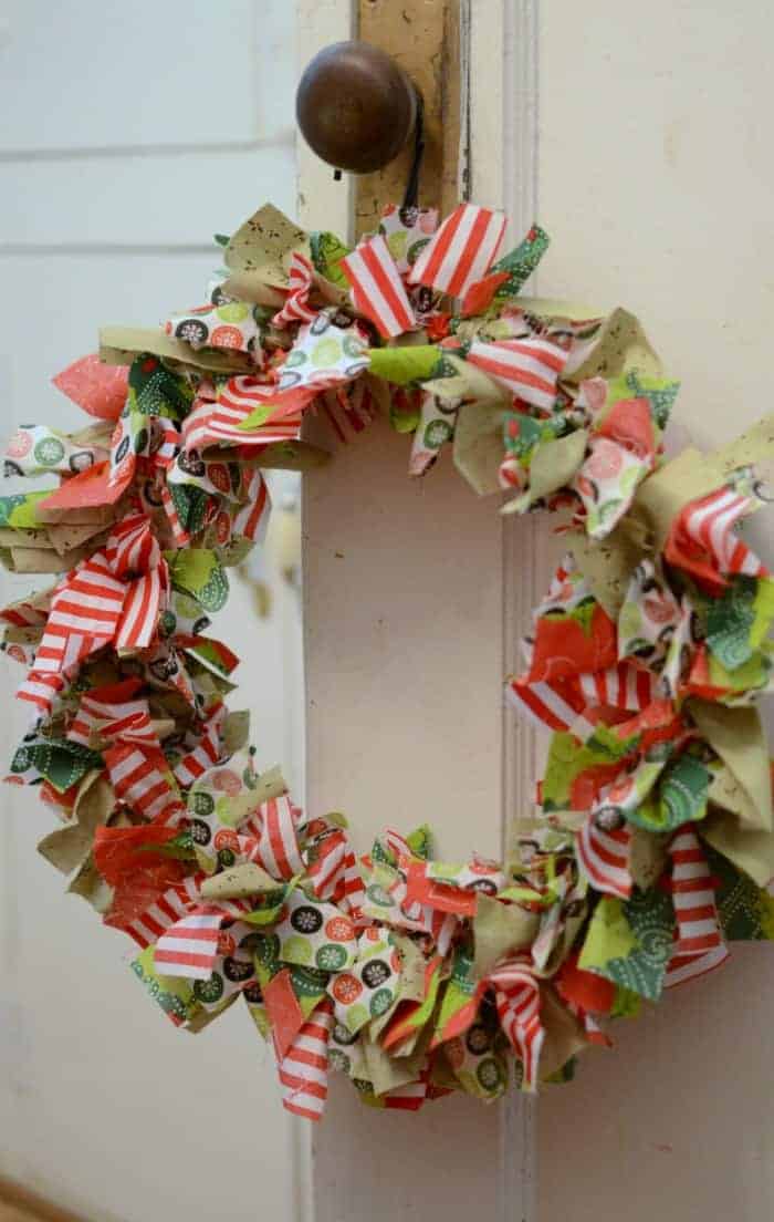 DIY Christmas Rag Wreath made from red, green, and white fabrics hanging on the doorknob of a white door.