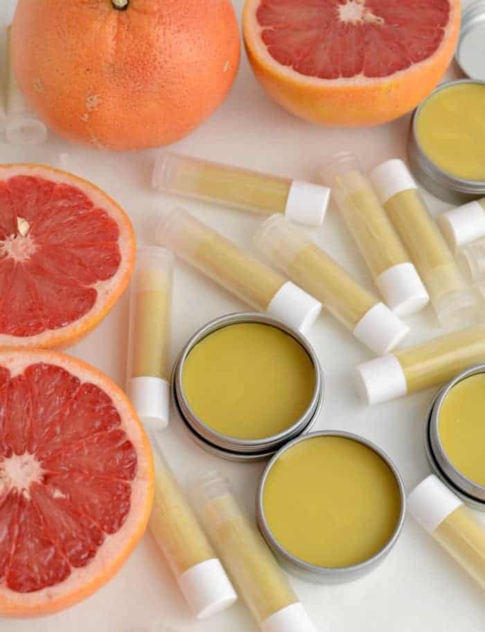 Close-up of homemade beeswax lip balm in lip balm tubs and small pots surrounded by grapefruits.