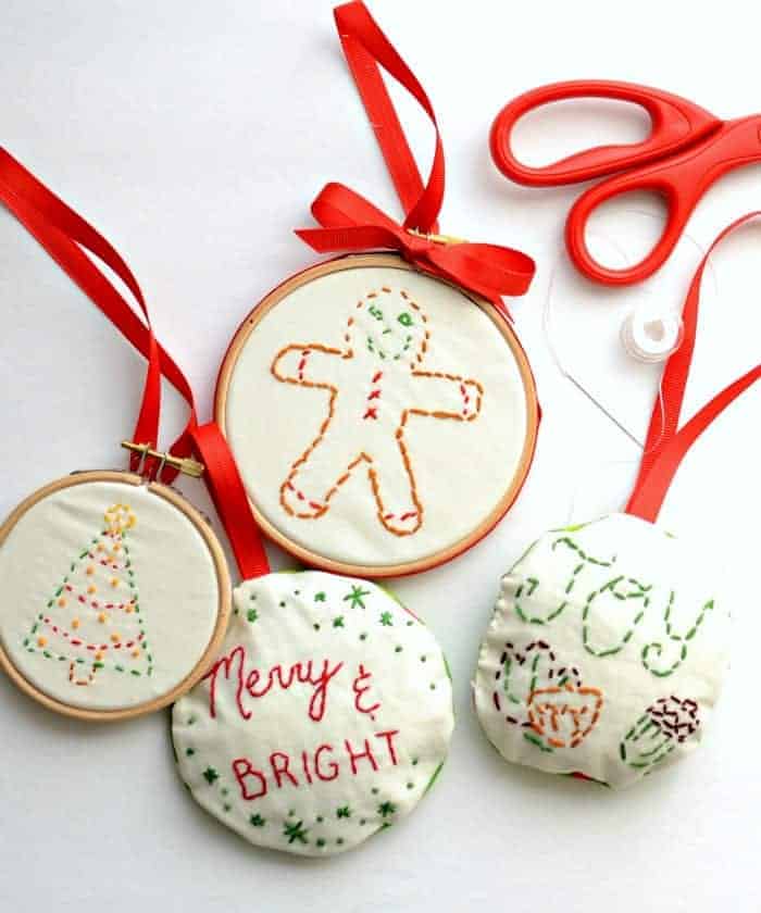 Four embroidered Christmas ornaments - two stuffed and two in hoops, a red-handled scissors, and needle and thread.