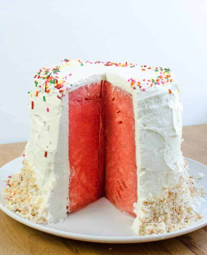 Watermelon Cake with Whipped Cream frosting on a white plate decorated with sprinkles and toasted coconut.