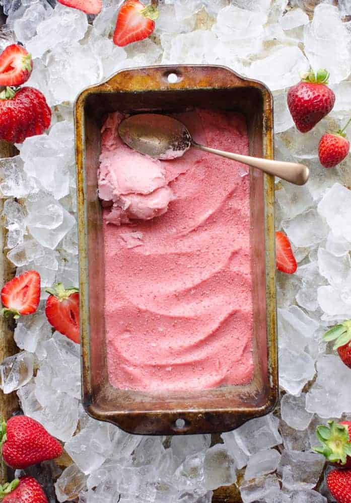 4 Ingredient Strawberry Frozen Yogurt in a loaf pan sitting on top of some ice surrounded by fresh strawberries.